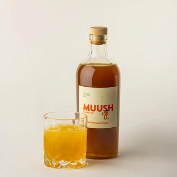 Bottle of Muush drink with a glass of orange juice on a light background