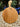 A round wooden serving board with a handle, standing upright on a gravel surface with potted plants in the background.