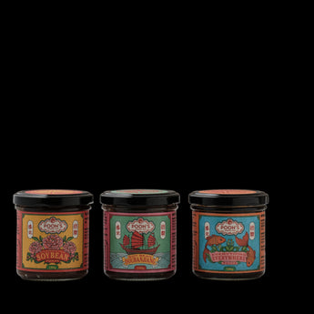 Three glass jars of Foon's condiments with black lids are lined up on a gray surface against a neutral beige background. The labels feature colorful illustrations for 'Foon's Soybean Paste', 'Foon's Sambal', and 'Foon's Curry Paste'.