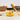 Jar of Welsh Honey Butter with a honey dipper on a table with fruit in the background