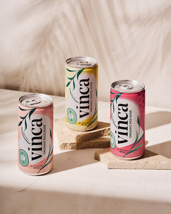Three cans of Vinca organic pink lemonade on a light background