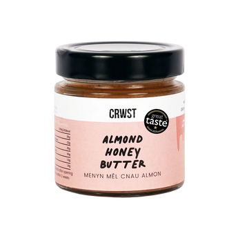 A jar of CRWST Almond Honey Butter with a black lid and a pink and white label, set against a solid pale green background.