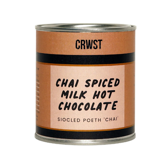 A cylindrical metal can of CRWST Chai Spiced Milk Hot Chocolate, featuring a terracotta-colored label with black text and stripes, set against a solid pale sage green background.