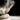 A person's hands sprinkling flour onto a ball of sourdough pizza dough on a surface with scattered flour particles, representing the ingredients of the kit.