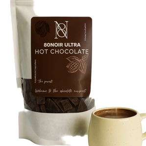 A stand-up pouch of 8onoir Ultra Hot Chocolate with a large dark brown label, shown next to a light beige ceramic mug filled with hot chocolate on a clean white background.