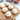 Wooden pizza peel with six pizza dough balls on a white surface with ingredients in bowls.