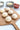 Wooden pizza peel with six pizza dough balls on a white surface with ingredients in bowls.
