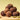 A pyramid of chocolate truffles dusted with cocoa powder sits on a wooden board, surrounded by whole walnuts, green cardamom pods, and dried figs against a soft yellow-green background.