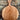 A round wooden serving board with a single handle and a hanging hole, leaning against a stone wall on gravel.
