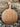 A round wooden serving board with a handle, leaning against a rustic stone wall on a bed of small gray pebbles.