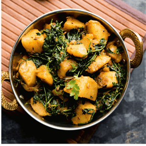 Bowl of Indian spiced  potato and spinach dish on a wooden surface