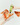 A person holds a bottle of TOS Pizza Sauce while another hand sprinkles the green sauce onto a slice of pizza. Other pizza slices are scattered on a clean white surface.