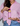 A woman wearing a pink button-up shirt and blue jeans holds a bottle of Toss Dressing hair color against a plain light gray background.