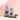 Two bags of CRWST Chocolate & Coconut Granola Cristas stand on a light surface against a soft peach-pink background, with chocolate pieces and white flakes placed beside them as styling props.