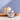 A tin of Crawst 55% Dark Hot Chocolate sits on a wooden board next to a ceramic mug filled with whipped cream and cocoa drips, with a spoon of chocolate garnish against a textured blue background.