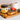 A jar of CRWST Welsh Honey Butter sits on a wooden board beside an open slice of toast topped with caramel, blueberries, and sliced strawberries, with a mug in the background.