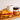 A jar of CRWST Welsh Sea Salted Caramel sits on a wooden board next to a croissant topped with fresh raspberries and drizzled caramel, with a white ceramic mug in the background.