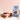 A stand-up pouch of CRWST Chocolate & Coconut Granola Clusters stands on a tabletop beside bowls of granola with berries and a mug against a soft pink textured wall.