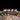 Four jars of Chimmy's hot sauces arranged on a rustic wooden block over a wooden table, with cilantro, peppercorns, and chili peppers as props against a black background.