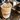 A close-up shot of espresso being poured from a portafilter into a brown paper coffee cup with a matching sleeve printed with the brand name 'CRWST'.