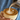 A close-up of a person pouring steamed milk from a metal pitcher into a ceramic cup of coffee with latte art, set against a blue striped shirt background.
