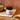 A jar of CRWST Almond Honey Butter sits on a wooden cutting board on a wooden table, styled with a rustic loaf of bread and a slice of toast spread with the honey butter in the foreground.