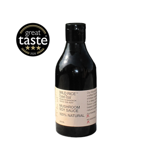 A bottle of Wild Rice Mushroom Soy Sauce on a light gray background, featuring a black bottle with a beige label and a 'great taste' rating badge on the left.