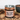 A metal tin of CRWST Chai Spiced Milk Hot Chocolate, styled on a wooden surface with scattered cocoa powder and a dark bowl of the hot chocolate in the background.