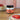 Jar of Welsh sea salted caramel on a wooden table with a bowl of strawberries and a plate of food in the background.
